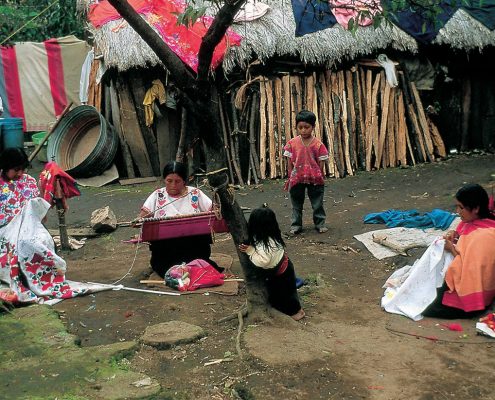 A woman kneels to weave, as a little girl looks on. Nabenchauk, 1991.